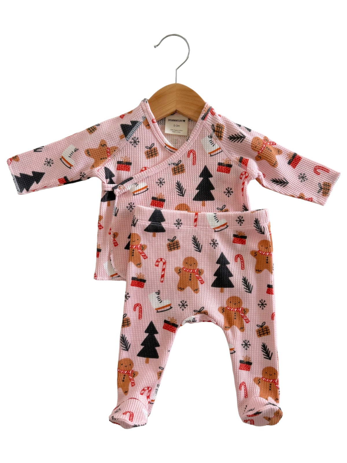 Pink baby outfit featuring gingerbread men, candy canes, and Christmas trees, hanging on a wooden hanger.