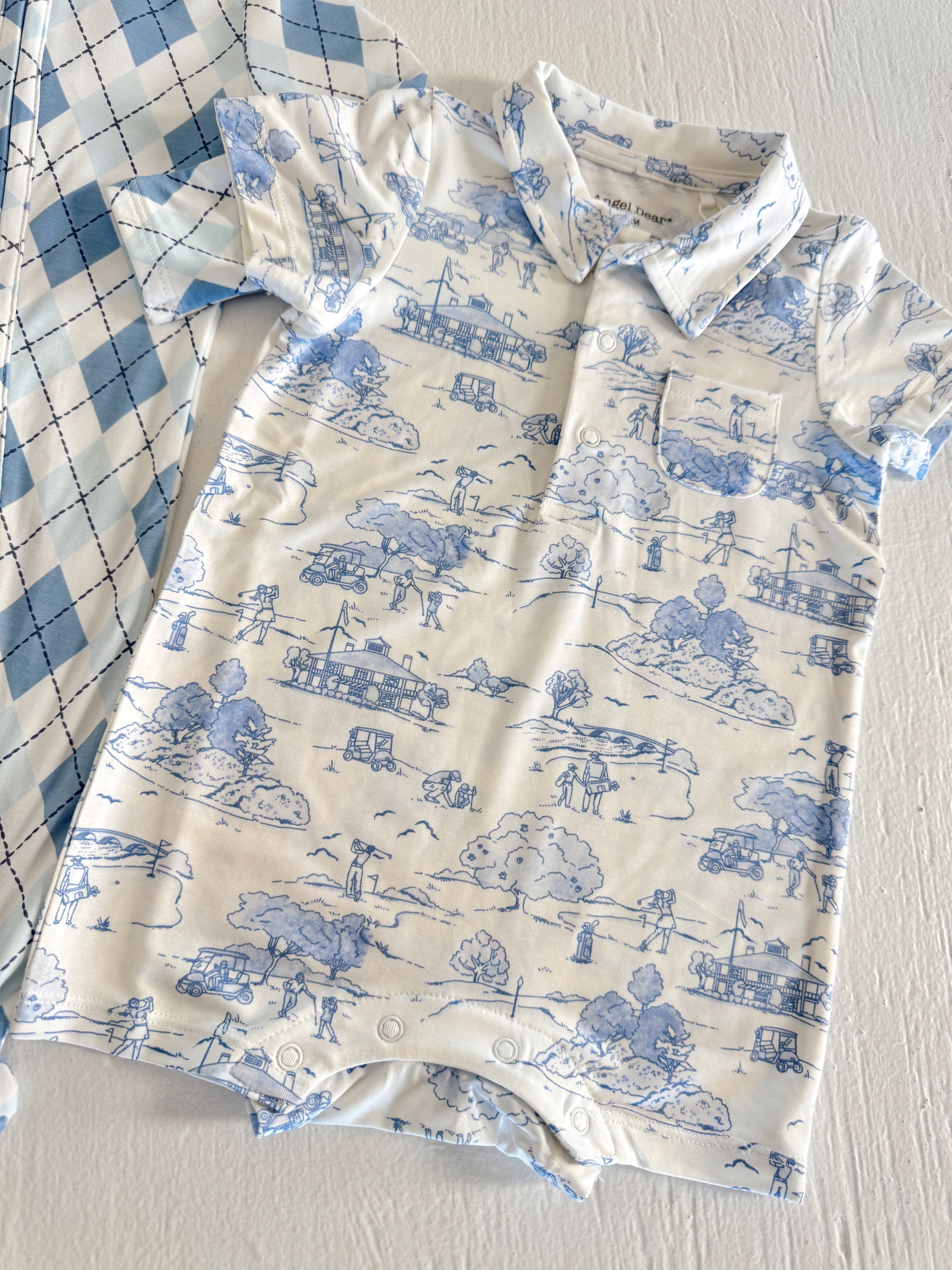 Blue and white children's romper with playful outdoor scenes, beside a blue plaid shirt.