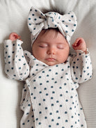 Sleeping baby wearing a floral onesie and a large bow headband on a cozy blanket.
