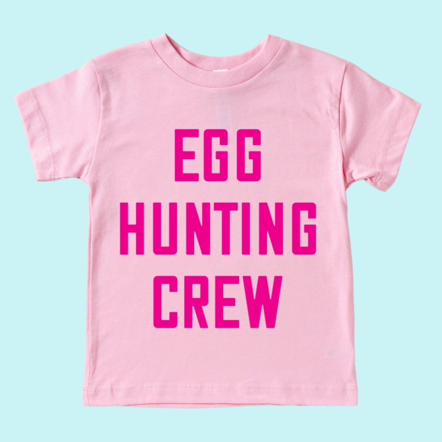 Pink t-shirt with bold text reading "EGG HUNTING CREW" on a light blue background.