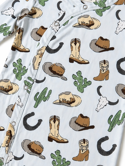 A light blue onesie with a western theme, featuring hats, boots, cacti, and cow skulls in playful patterns.