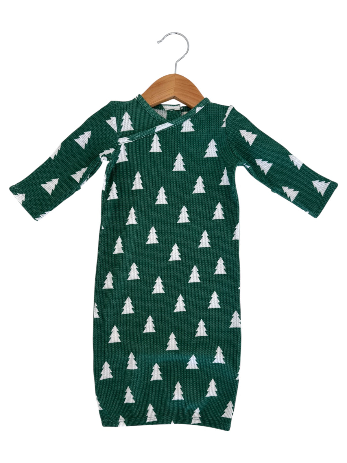 Green baby outfit with white tree patterns, hanging on a wooden hanger.