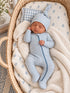 Newborn baby asleep in a cozy bassinet, dressed in blue and white striped sleeper with a matching hat.