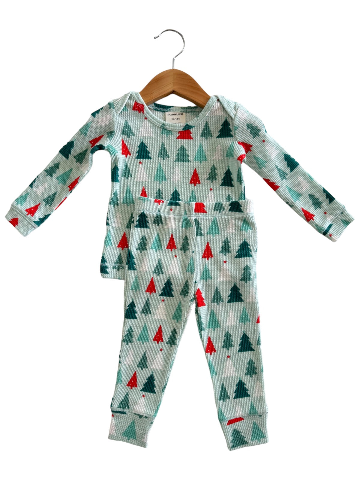 Child's holiday-themed pajama set featuring green and red trees on a light background, displayed on a hanger.