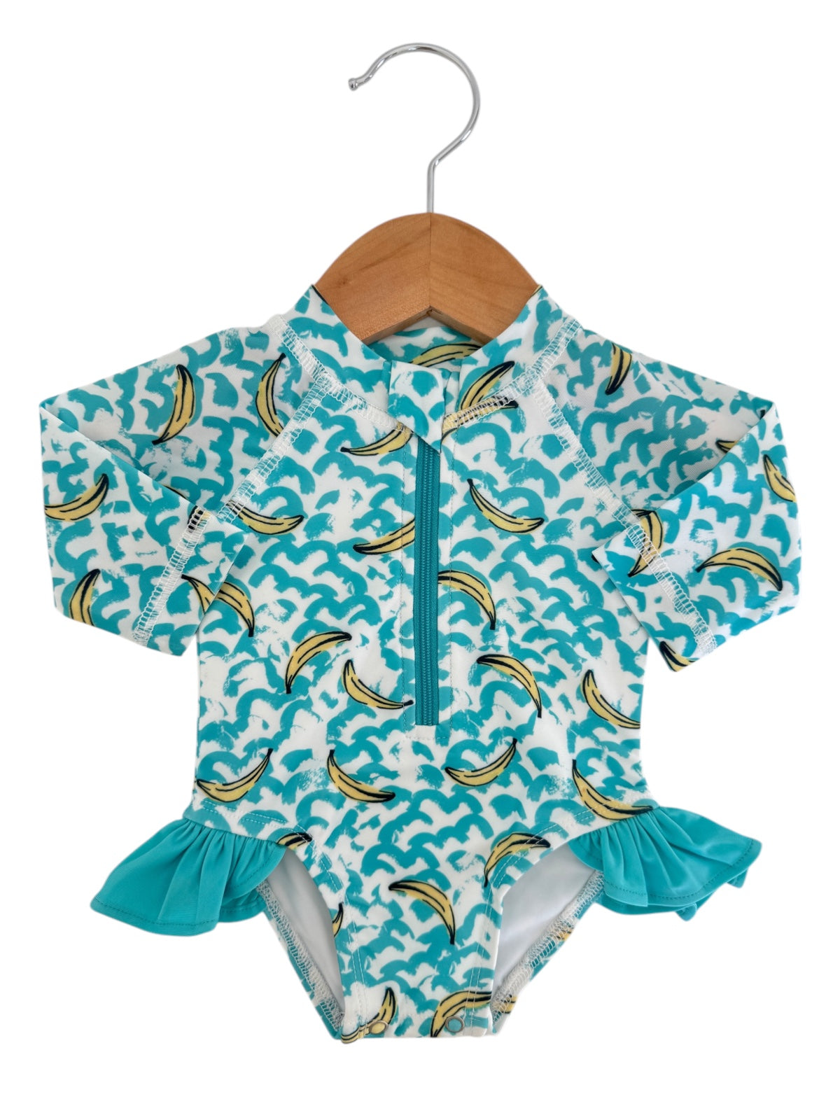 Children's swimwear featuring a wave and banana print, long sleeves, and a ruffled hem, hung on a wooden hanger.