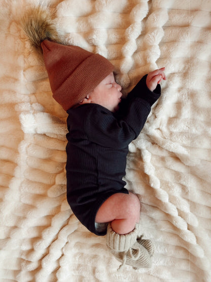 Newborn baby sleeping on a fluffy blanket, wearing a brown hat and knitted booties.