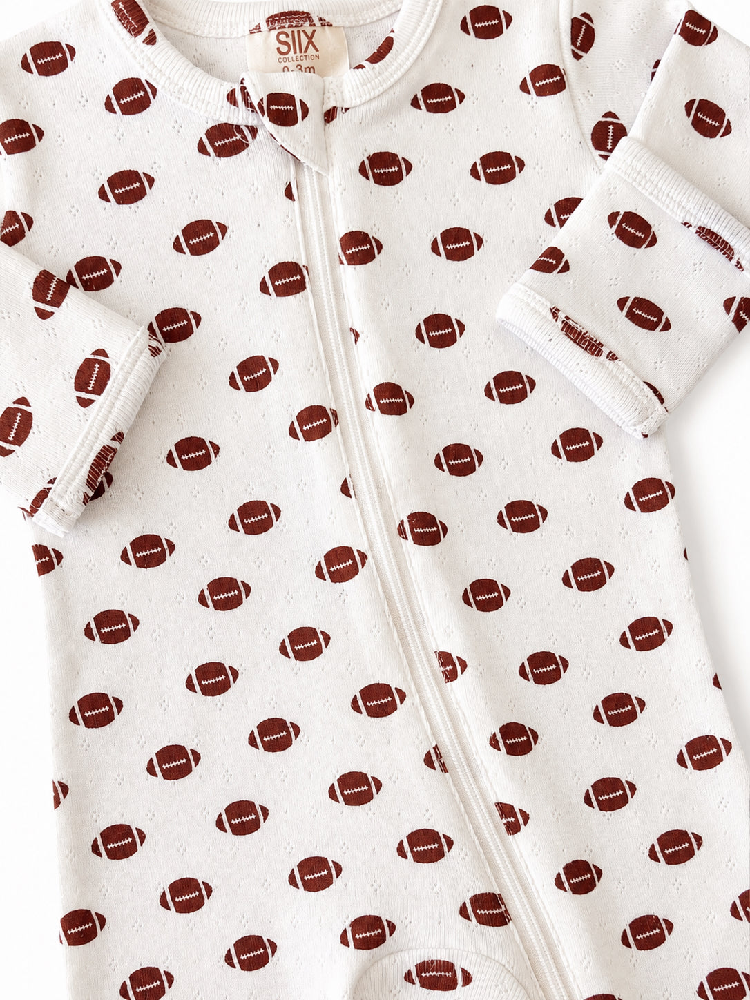White baby onesie with a football pattern, featuring a zipper and soft cuffs. Ideal for infants aged 0-3 months.