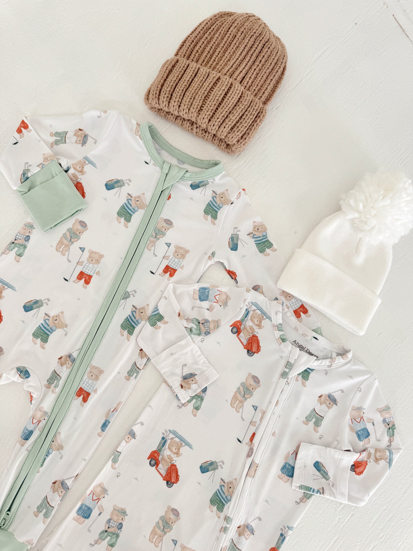 Two baby onesies with bear prints and two cozy hats, one beige and one white, on a light background.