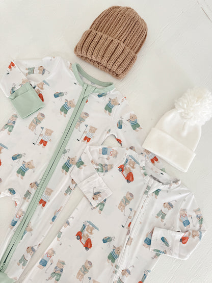 Two baby onesies with bear prints and two cozy hats, one beige and one white, on a light background.
