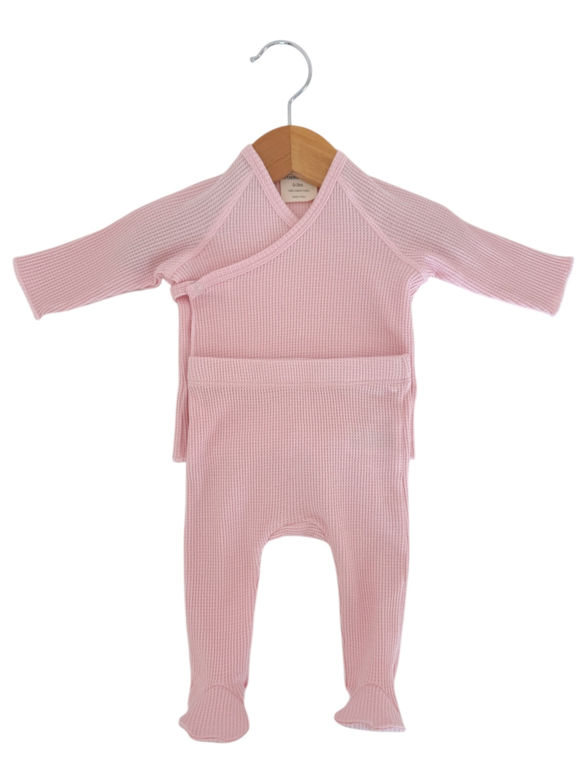 Baby pink wrap-style outfit with long sleeves and footed pants, hanging on a wooden hanger.