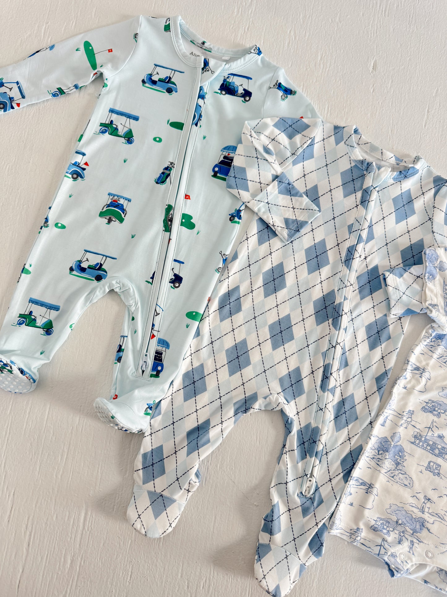 Two baby onesies in blue designs: one with golf carts, the other in a blue argyle pattern on a white background.