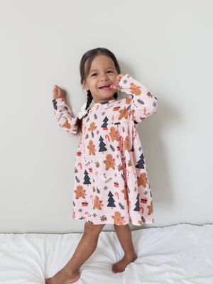 Smiling girl in a gingerbread dress, posing playfully against a neutral background.
