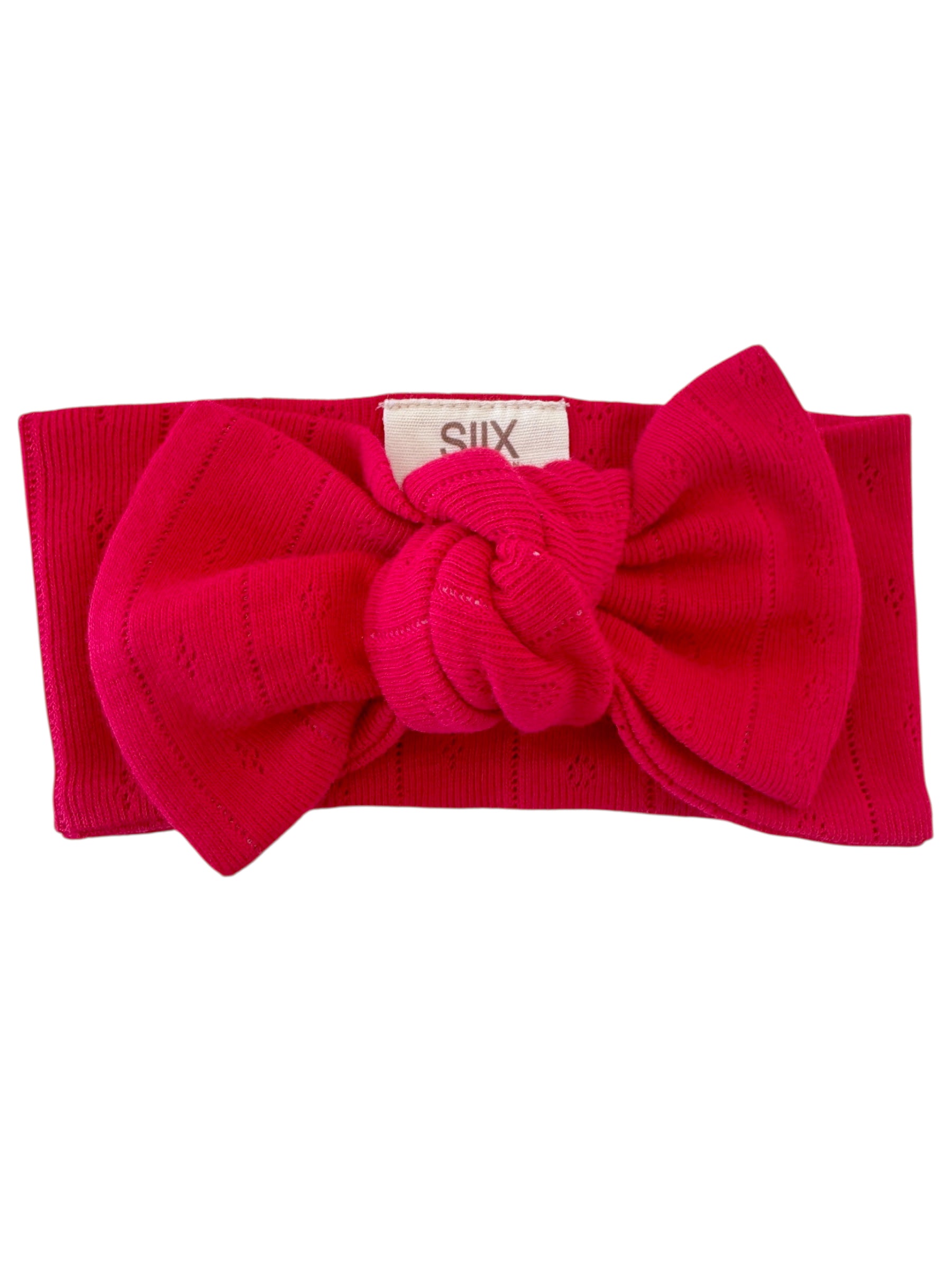 Bright pink headband with a large knot detail, featuring a textured ribbed design and a small tag marked "SIX."