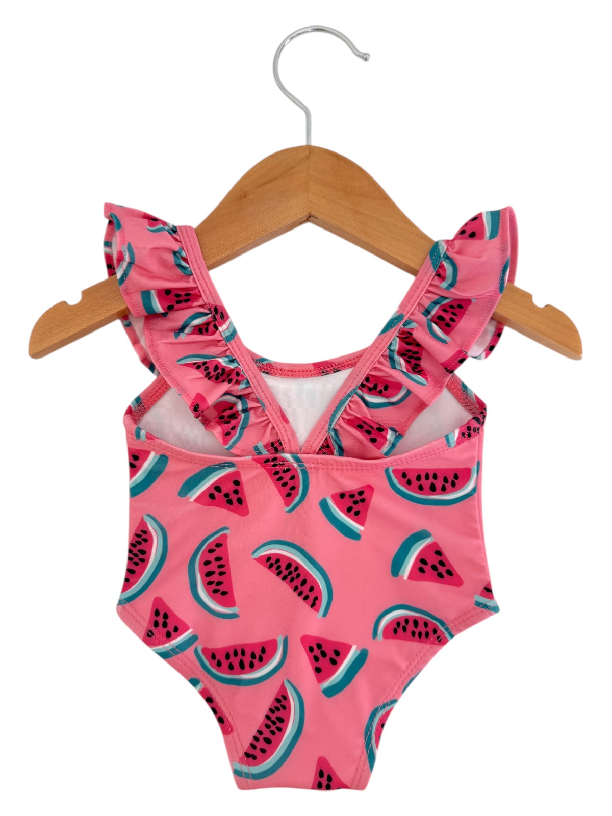 Girls' pink swimsuit with ruffles and watermelon slice pattern, hanging on a wooden hanger.