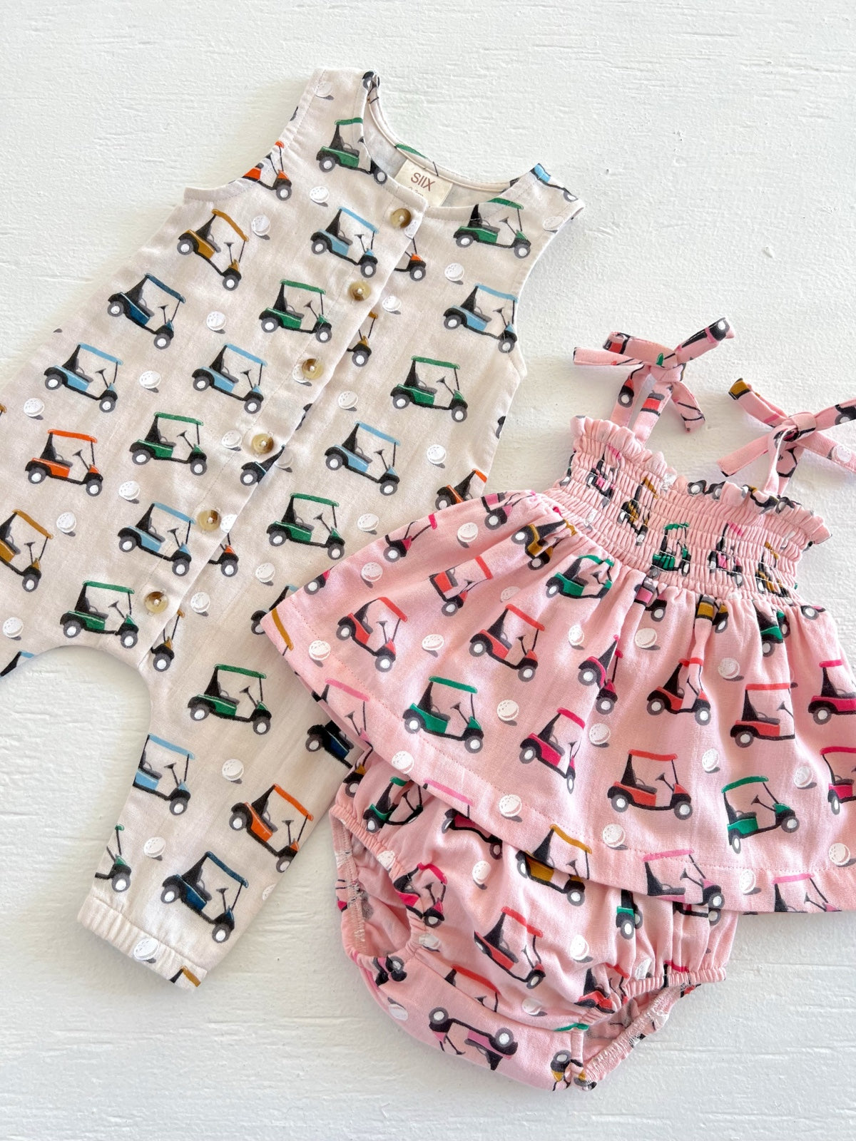 Two infants' outfits featuring playful golf cart patterns: a romper and a pink dress with matching bloomers.
