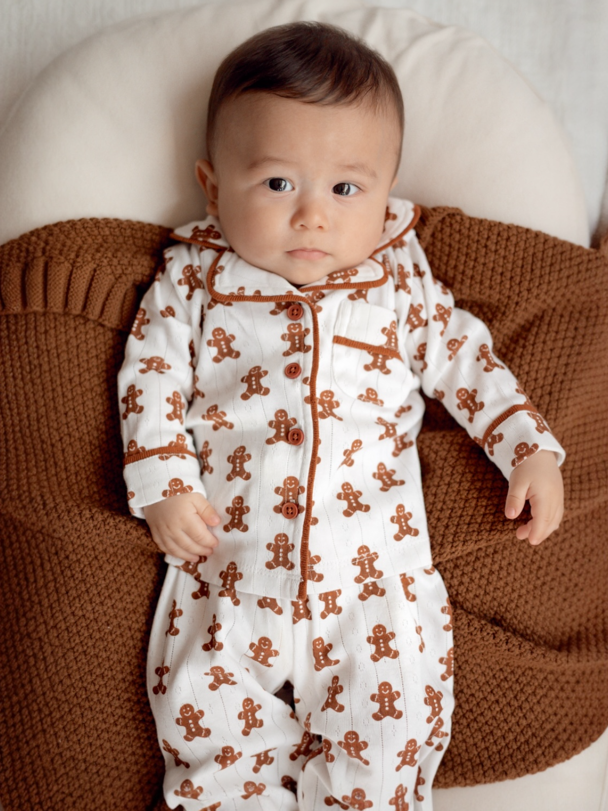 Baby in gingerbread-themed pajamas lying on a cozy, textured blanket.