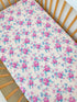 Floral crib sheet with pink roses and blue accents on a light background, displayed in a wooden crib.