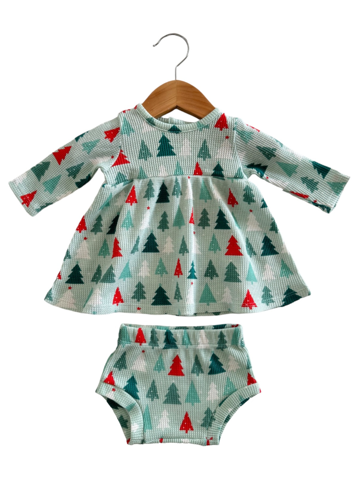 Light blue dress with green and red trees, paired with matching bloomers, hanging on a wooden hanger.