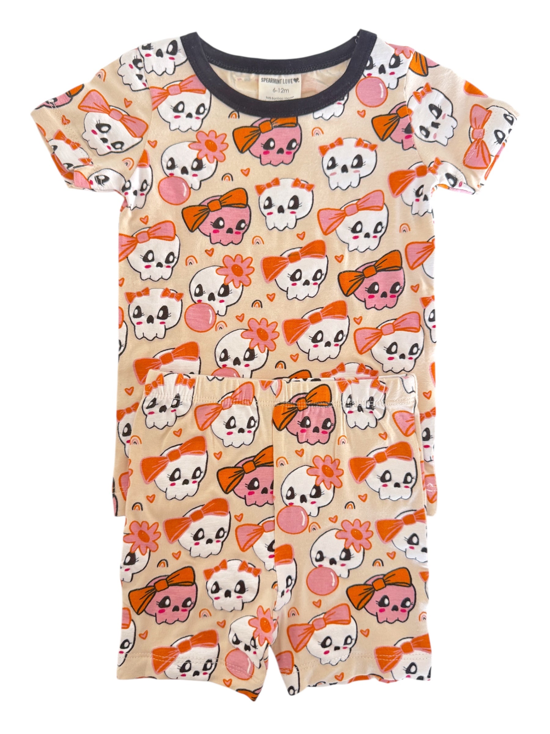 Child's short-sleeve pajama set featuring colorful skulls with bows and flowers on a beige background.
