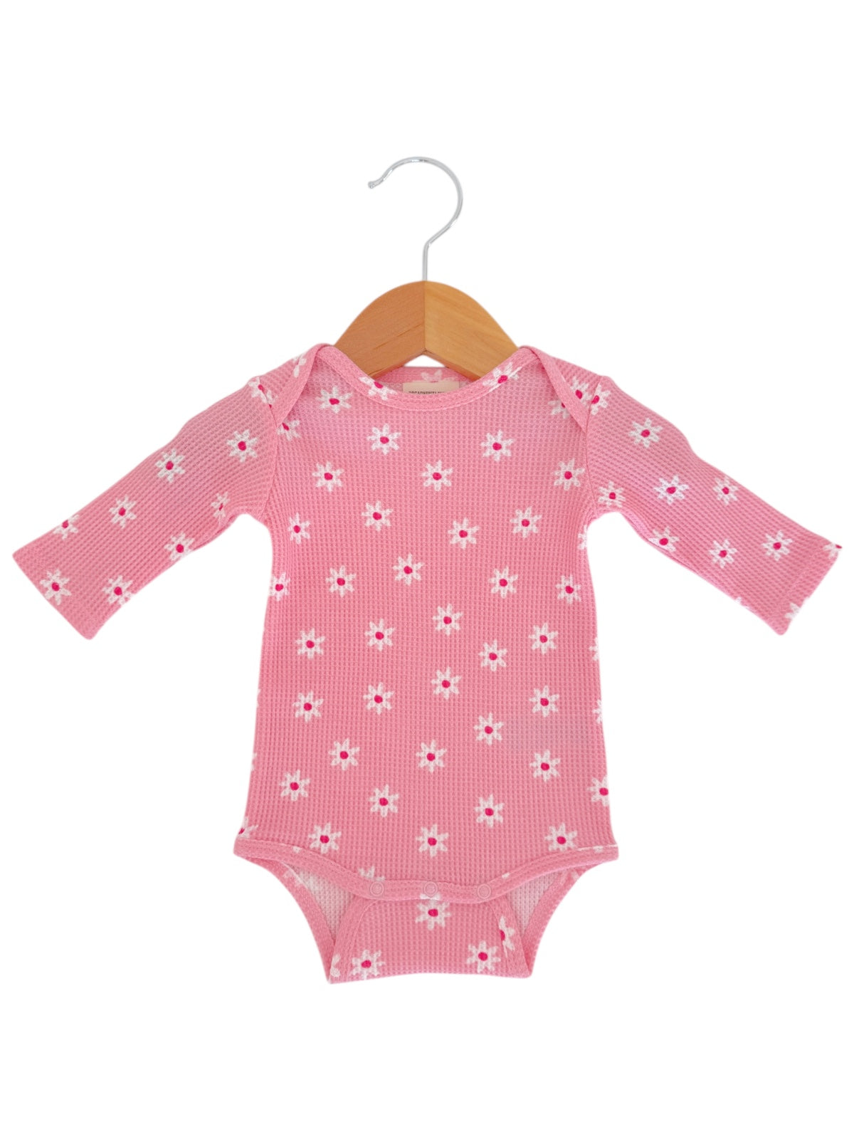 Pink baby onesie with long sleeves and floral pattern, displayed on a wooden hanger.