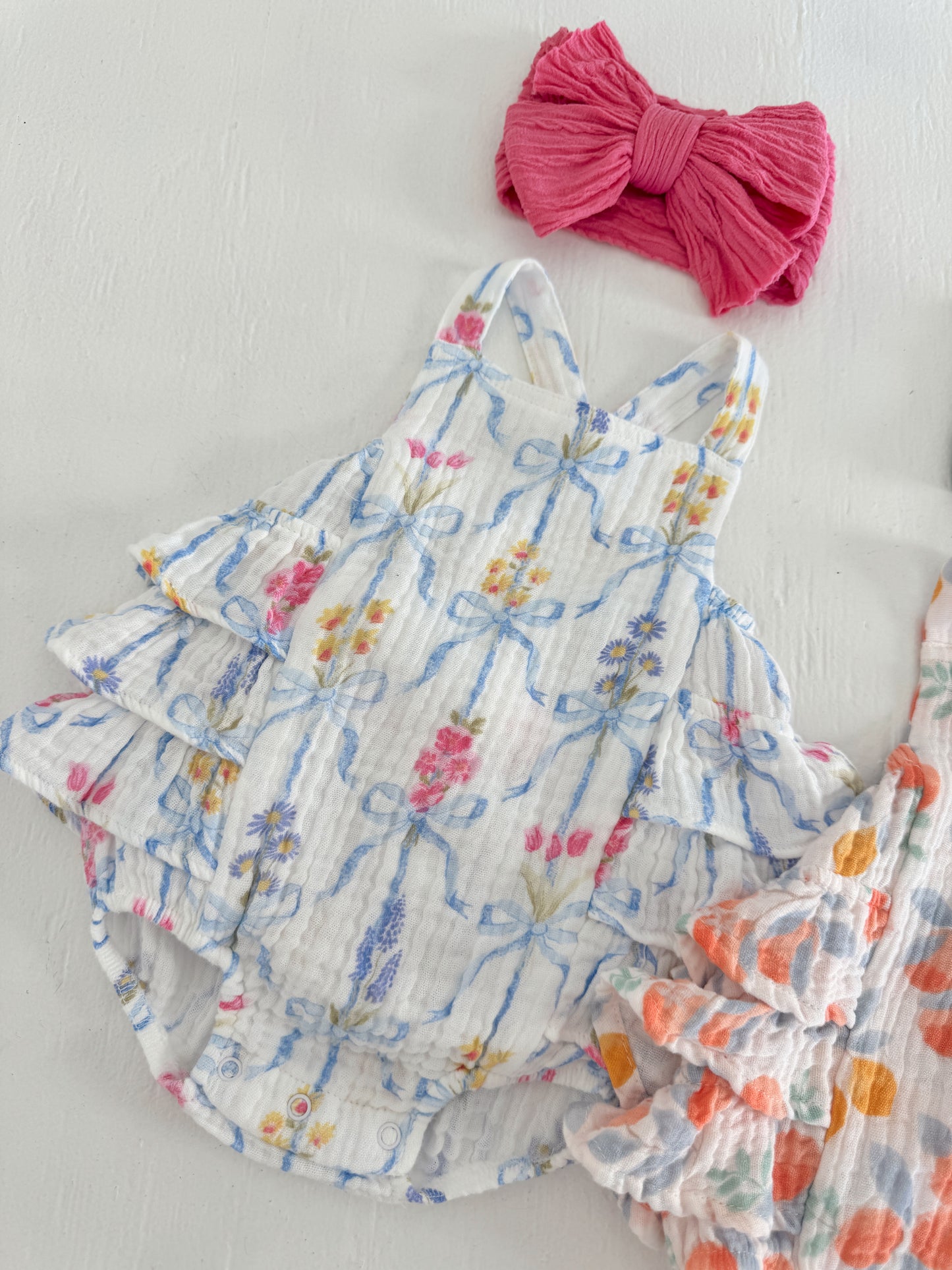 Floral tiered baby romper with a pink bow headband on a light background.
