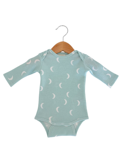 Light blue long-sleeve baby bodysuit with crescent moon patterns, displayed on a wooden hanger.
