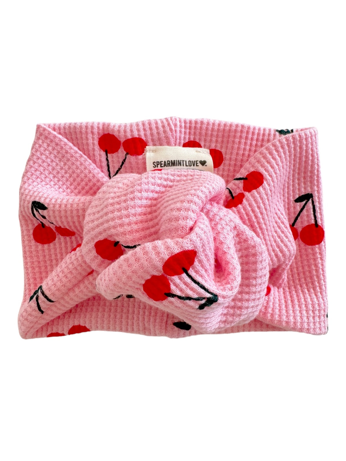 Pink headband with cherry print, featuring a knot and a tag that says "SPEARMINTLOVE."