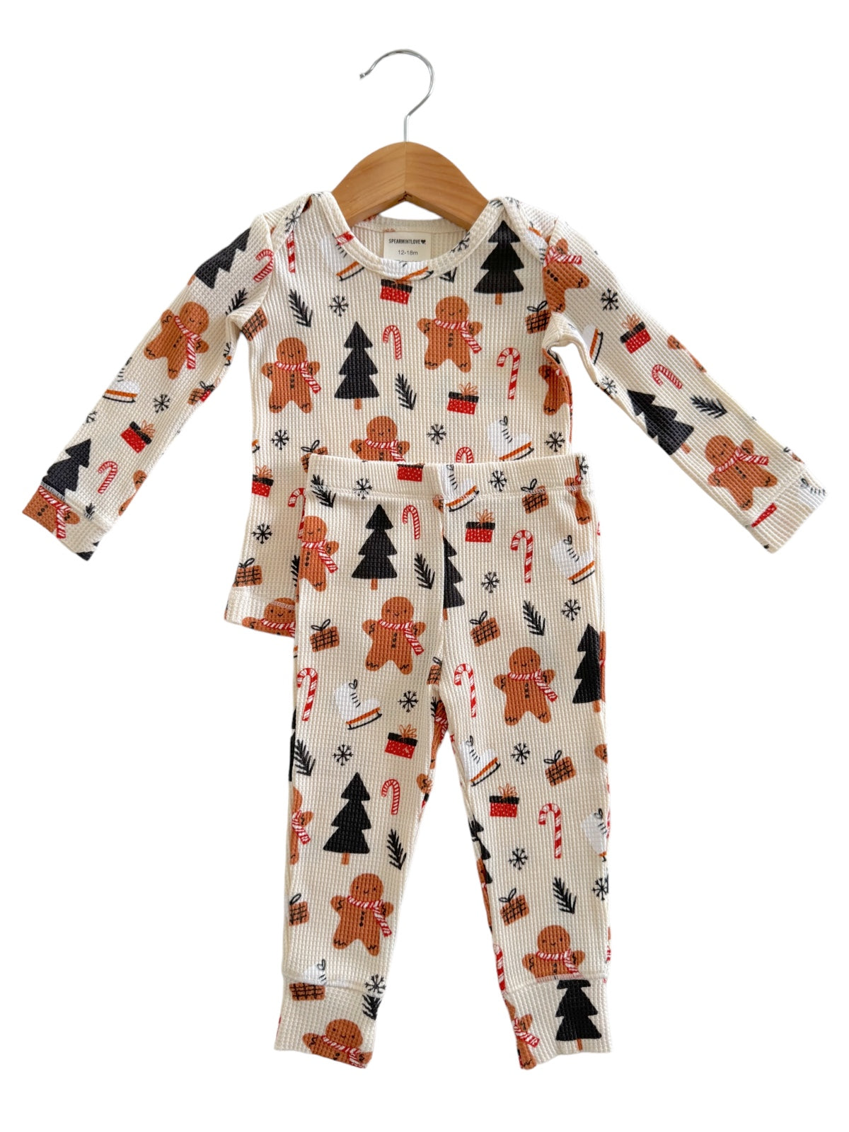 Children's holiday pajamas with gingerbread men, candy canes, and Christmas trees on a cream background.