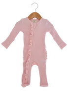 Pink baby onesie with ruffle details, featuring long sleeves and a front zipper, hanging on a wooden hanger.
