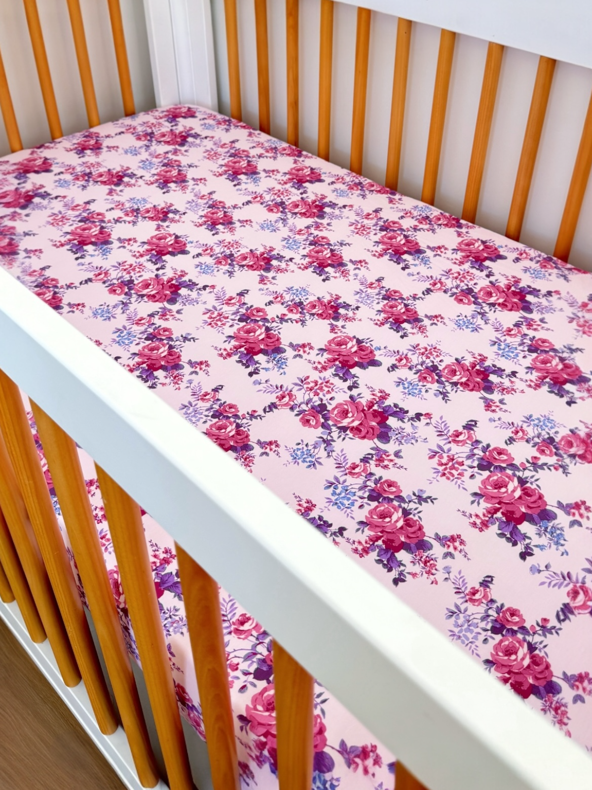 Floral crib sheet in a wooden crib with pink background and colorful roses.