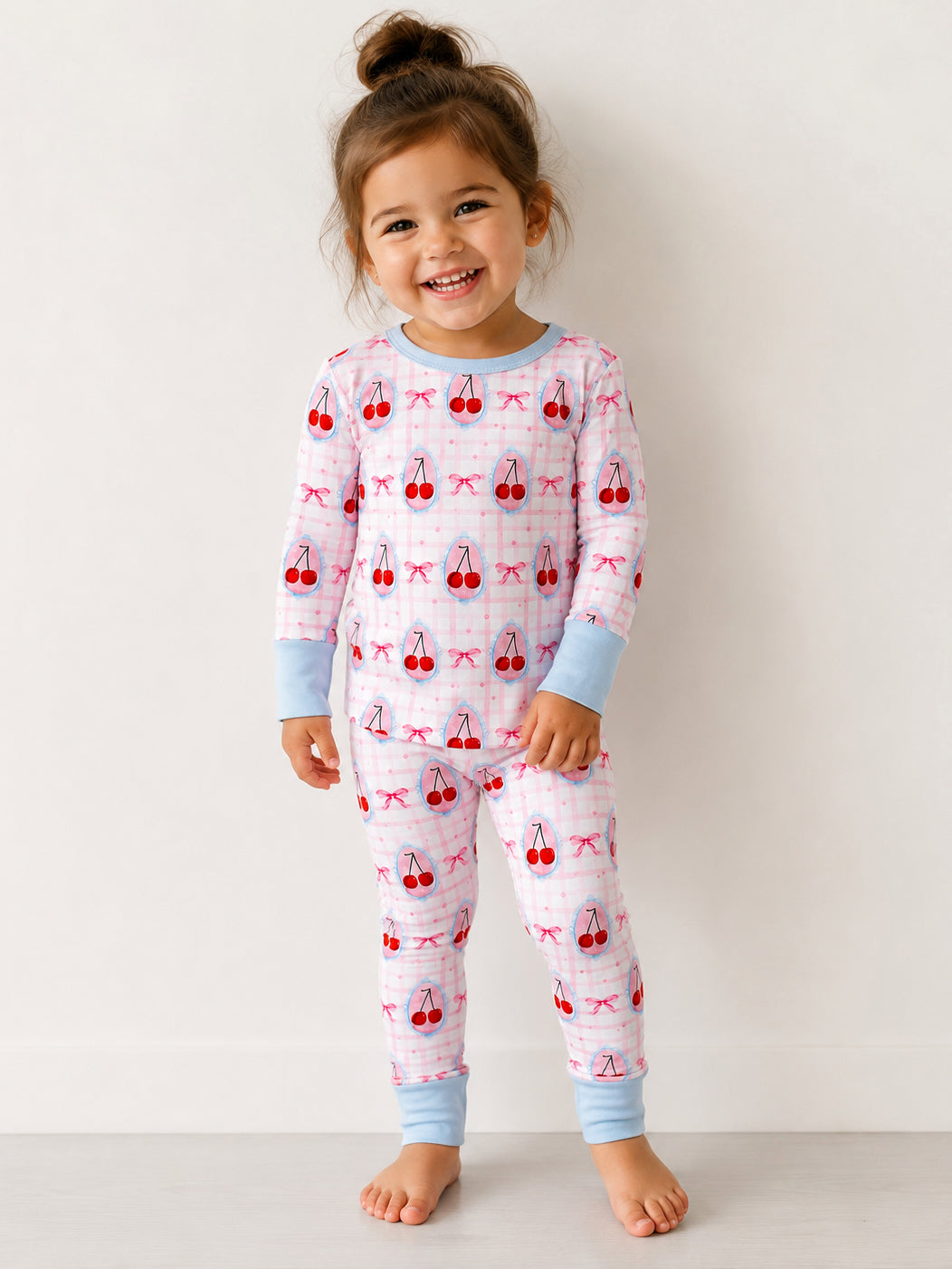 Smiling child in playful cherry-patterned pajamas, standing on a light background.