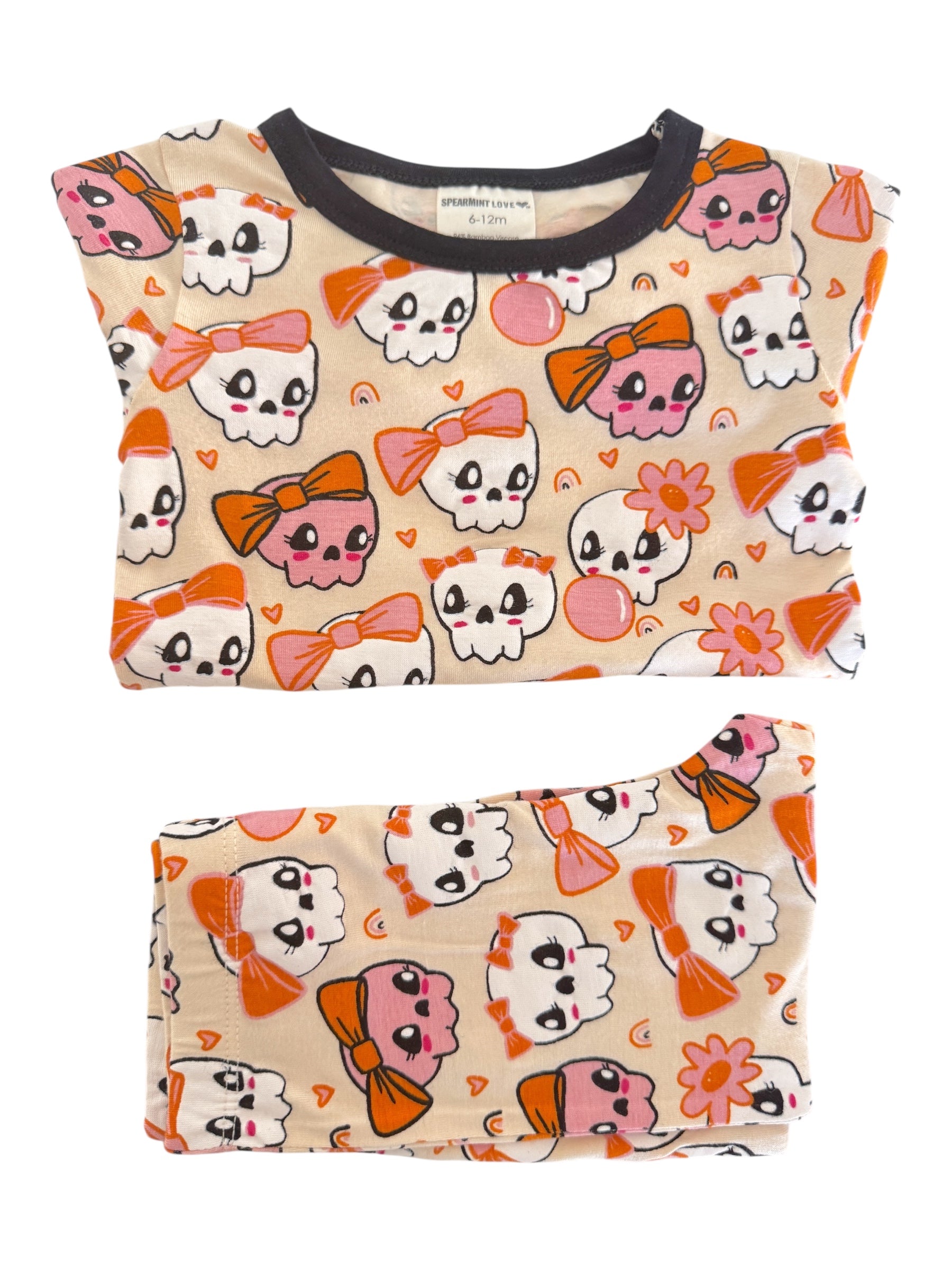 Kids' pajamas featuring playful skull designs with bows in pink and orange on a soft beige background.