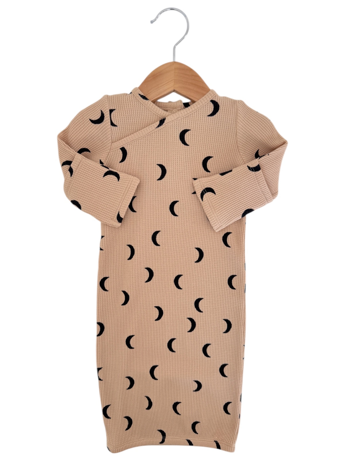 Beige baby dress with black crescent moon pattern, hanging on a wooden hanger against a white background.