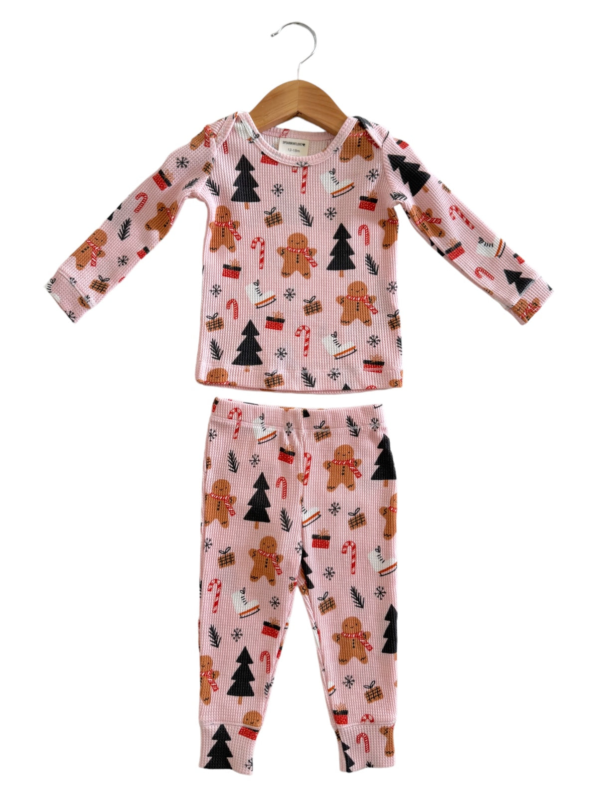Holiday-themed children's pajamas with gingerbread, candy canes, and Christmas trees, on a pink background.
