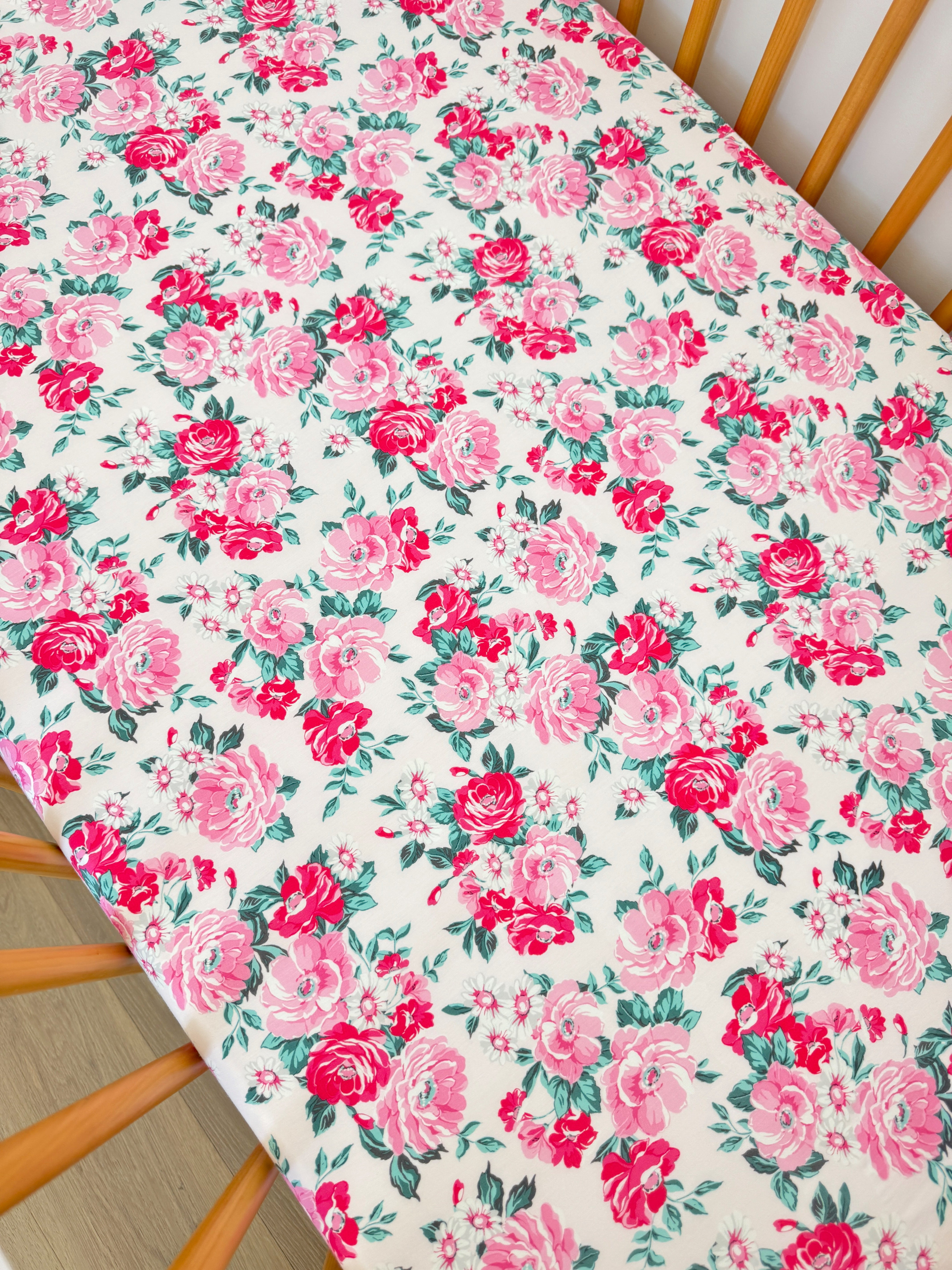 Floral tablecloth with pink roses and green leaves on a light background, draped over a wooden chair.