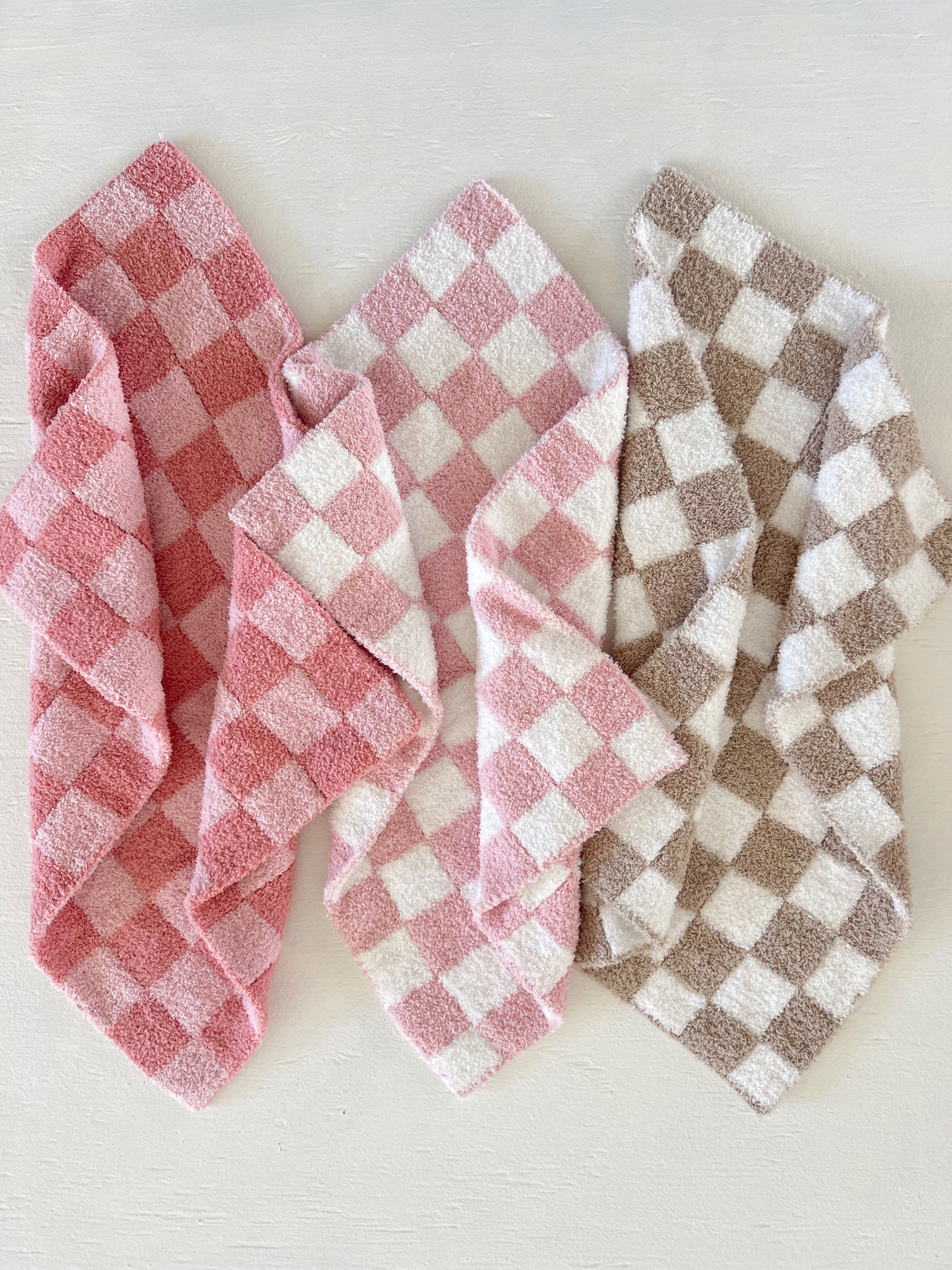 Three folded checkered towels in pink, white, and brown on a light background.