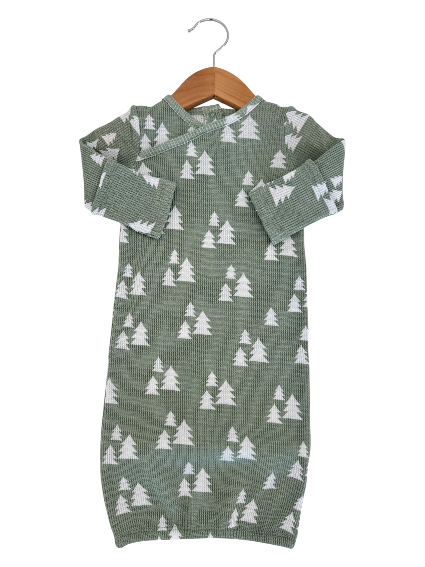 Green infant outfit with white tree pattern, hanging on a wooden hanger against a white background.