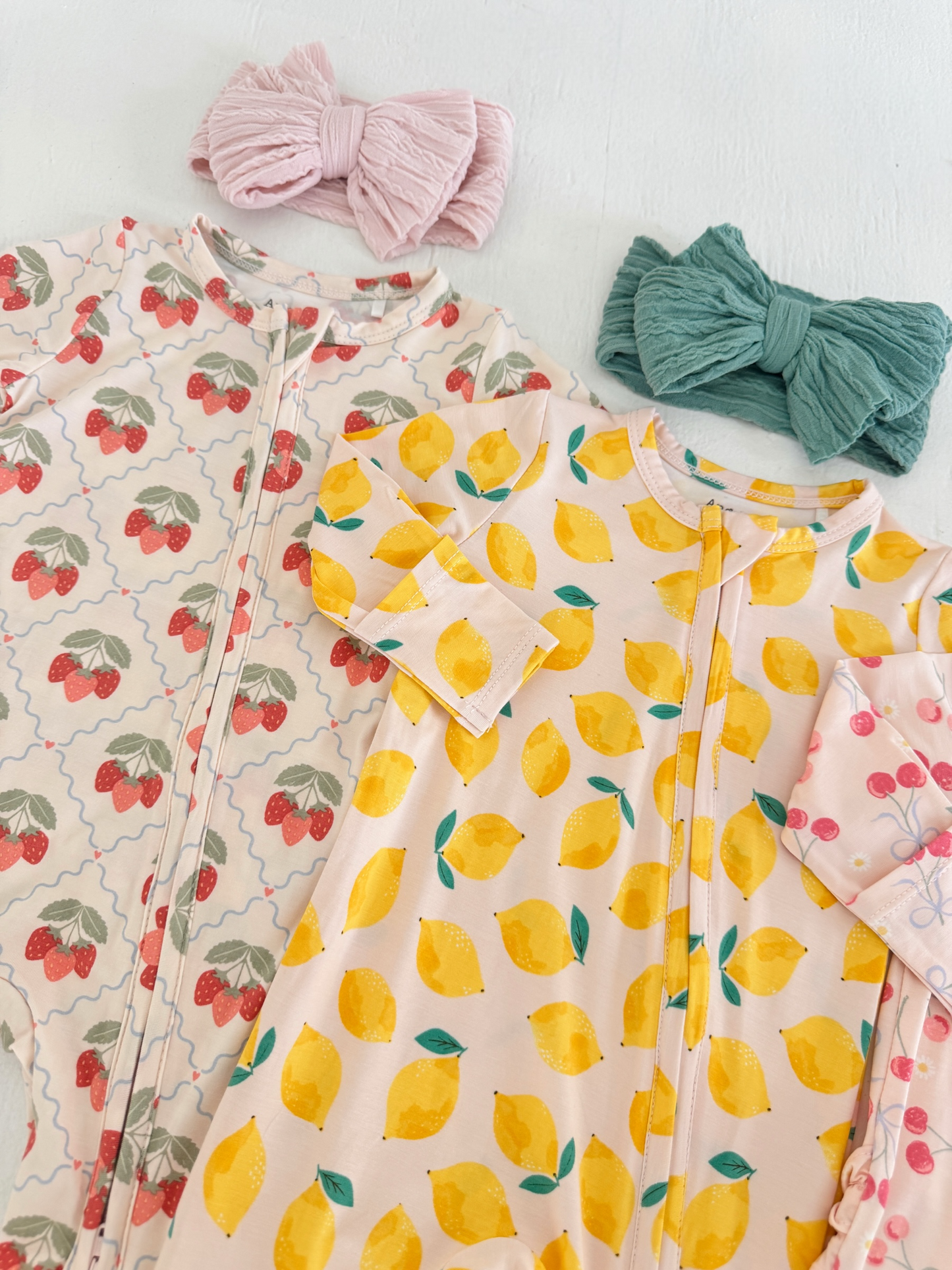 Children's outfits featuring strawberry and lemon patterns, paired with soft headbands in pink and teal.
