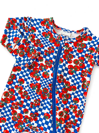 Colorful toddler swim onesie with red tomatoes and blue checkered pattern, featuring a front zipper.