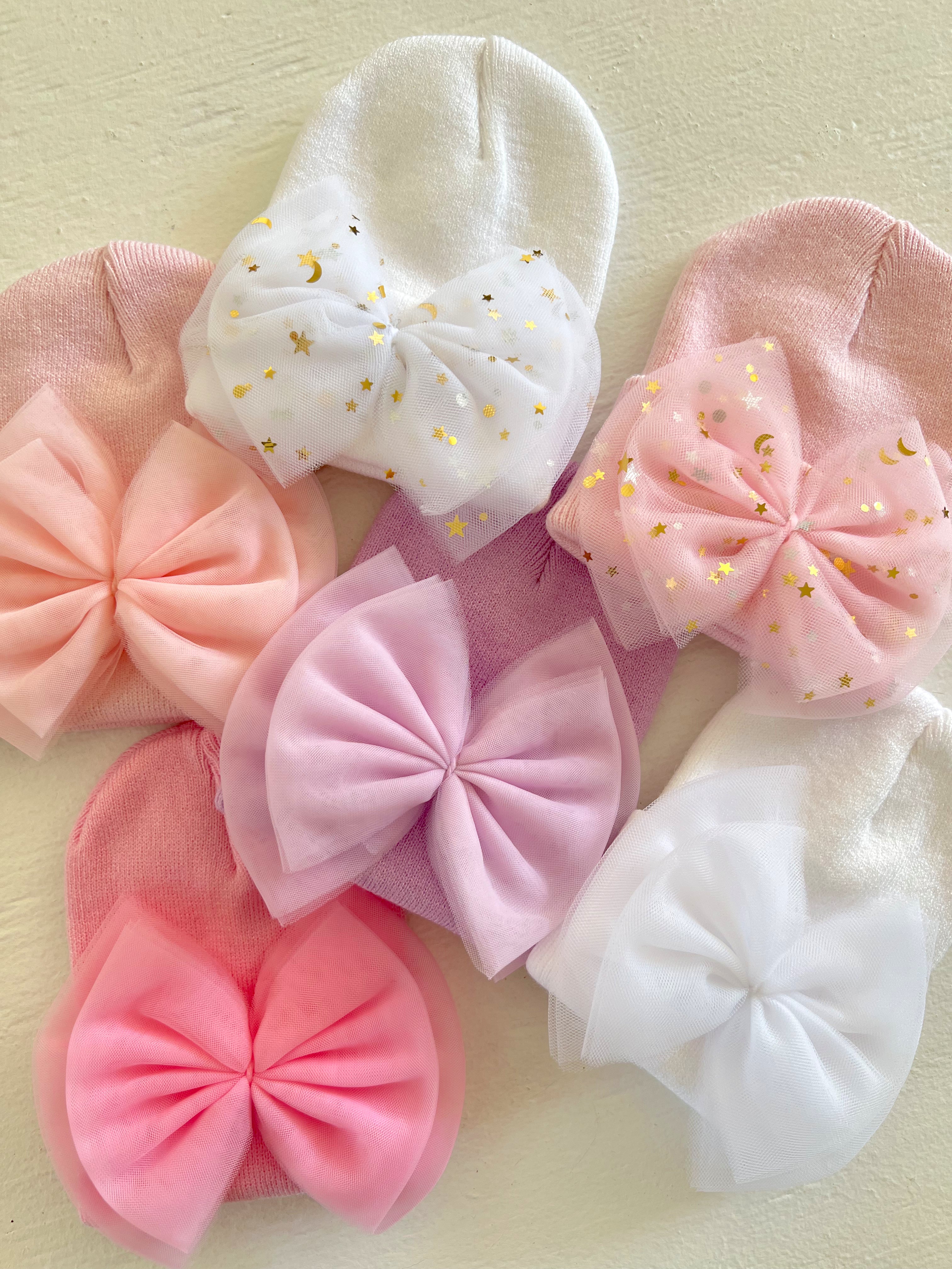 Assorted baby hats with large bows in pink, white, and pastel shades, featuring star and moon patterns.