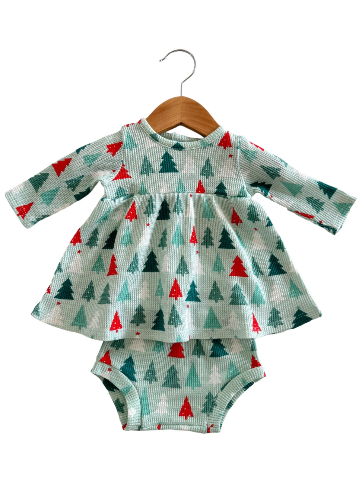 Baby dress with long sleeves, green and red tree pattern, on a wooden hanger, paired with matching bloomers.