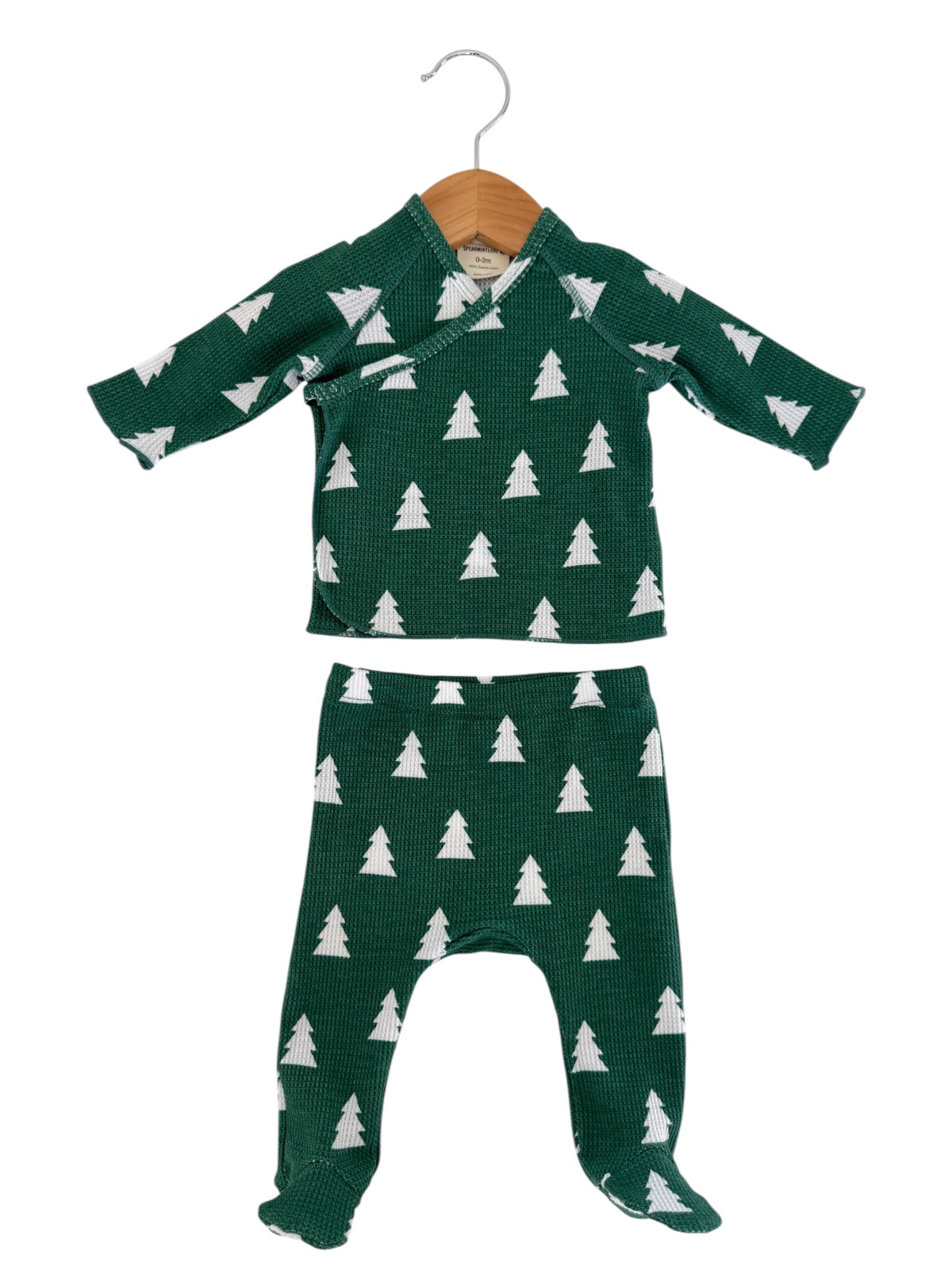 Green baby outfit with white tree patterns, featuring a wrap top and matching pants, hanging on a wooden hanger.