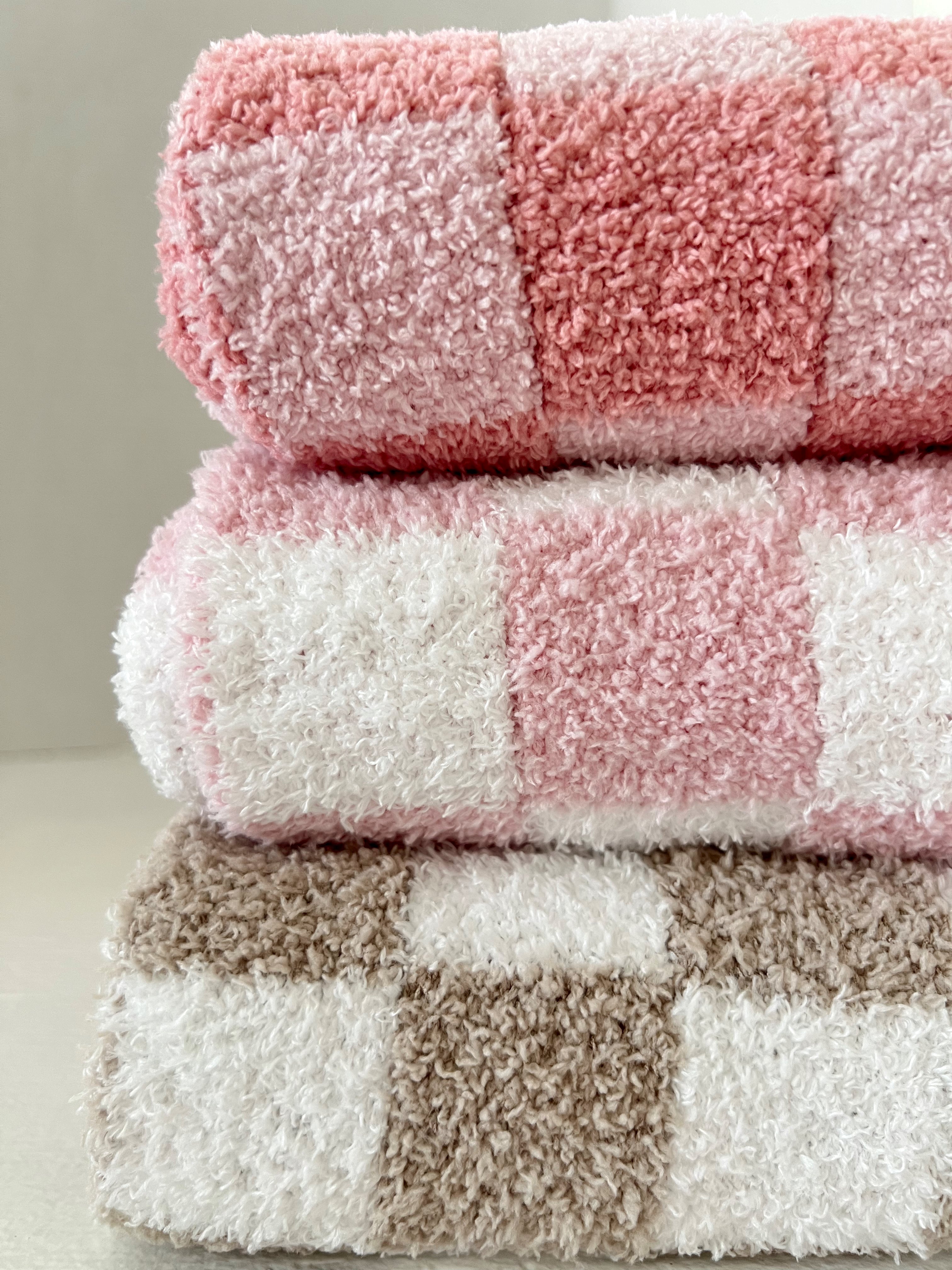 Three stacked towels in pink, white, and tan plaid patterns, showcasing soft textures and bright colors.