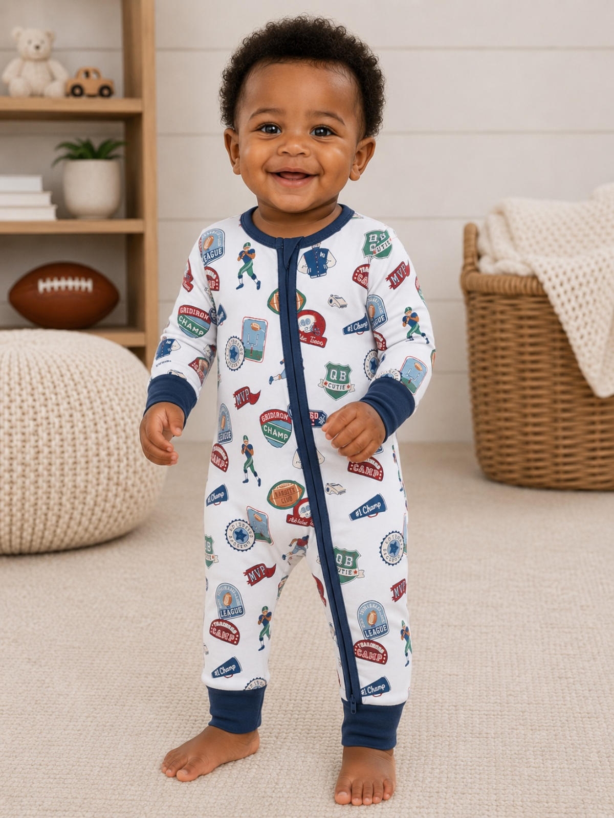 Smiling toddler in football-themed pajamas, standing on a carpeted floor, with toys and decor in the background.