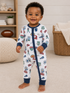 Smiling toddler in football-themed pajamas, standing on a carpeted floor, with toys and decor in the background.