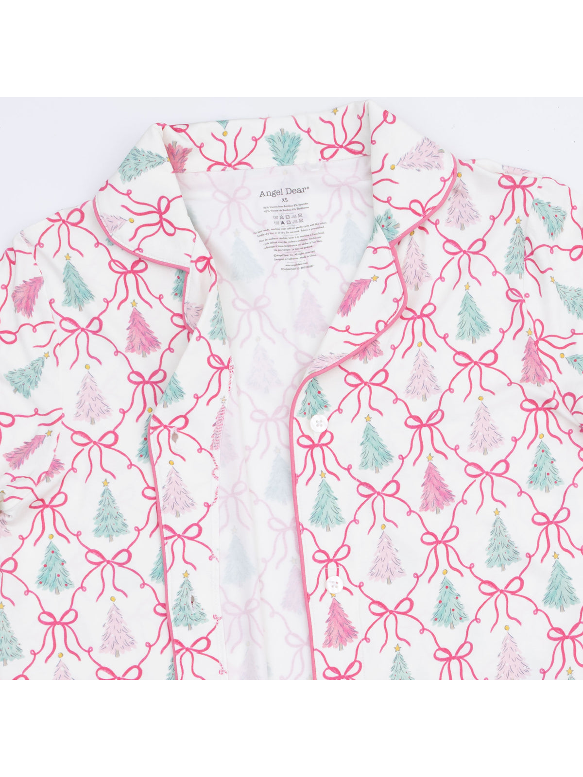 White shirt with pink bows and colorful Christmas trees, showcasing a festive pattern and a tag inside.