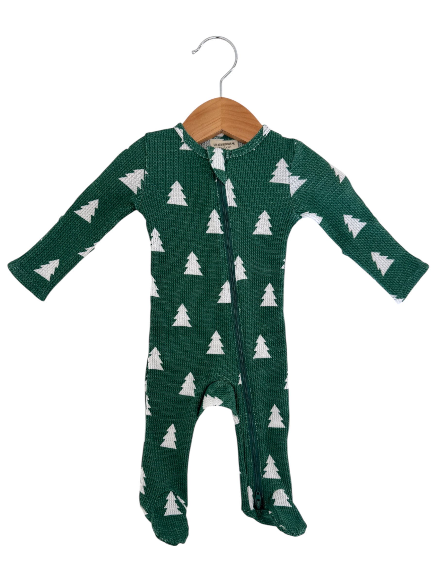 Green baby onesie with white pine tree pattern, featuring a front zipper and long sleeves, displayed on a wooden hanger.