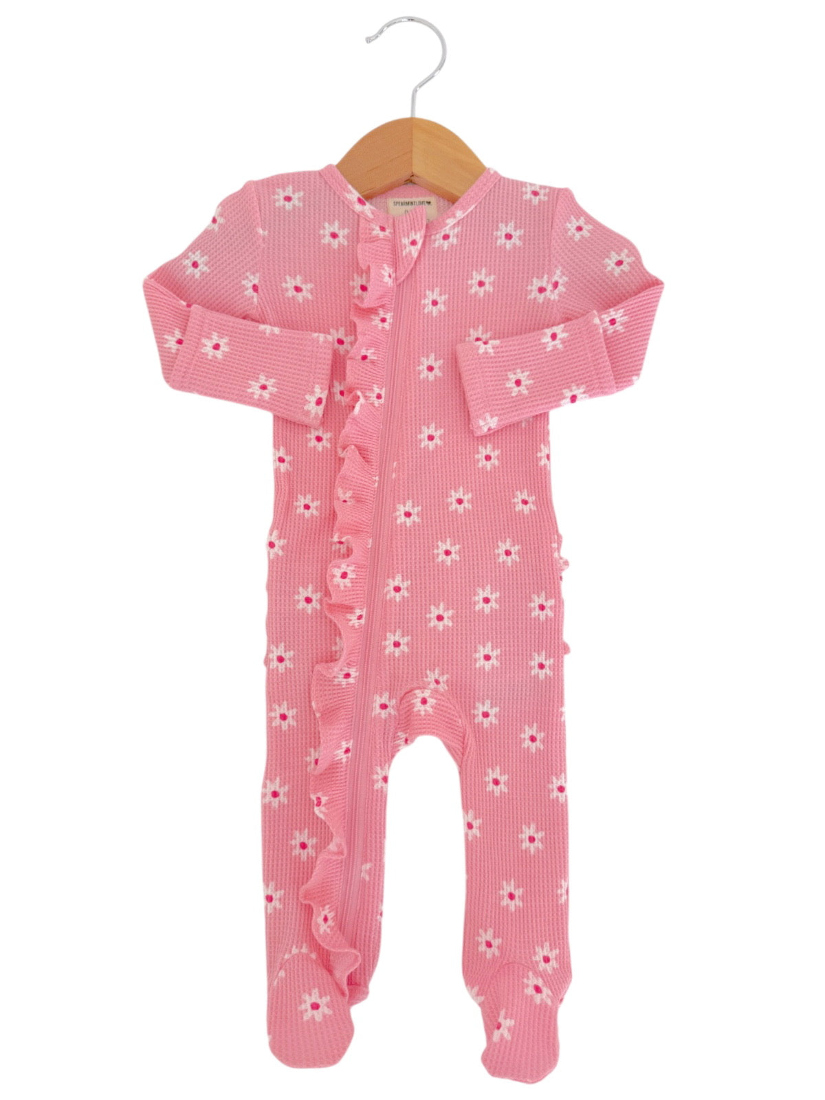 Pink baby onesie with ruffled detail and white flower patterns, hanging on a wooden hanger.