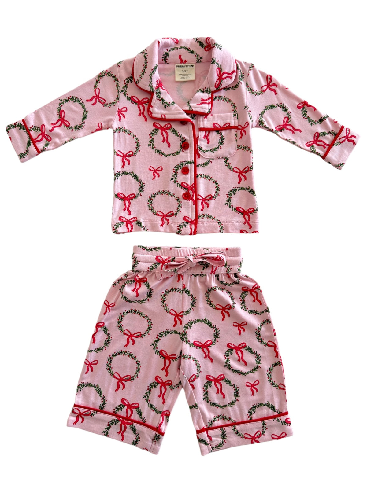 Pink children's pajama set featuring holiday wreaths and bows in red and green patterns.