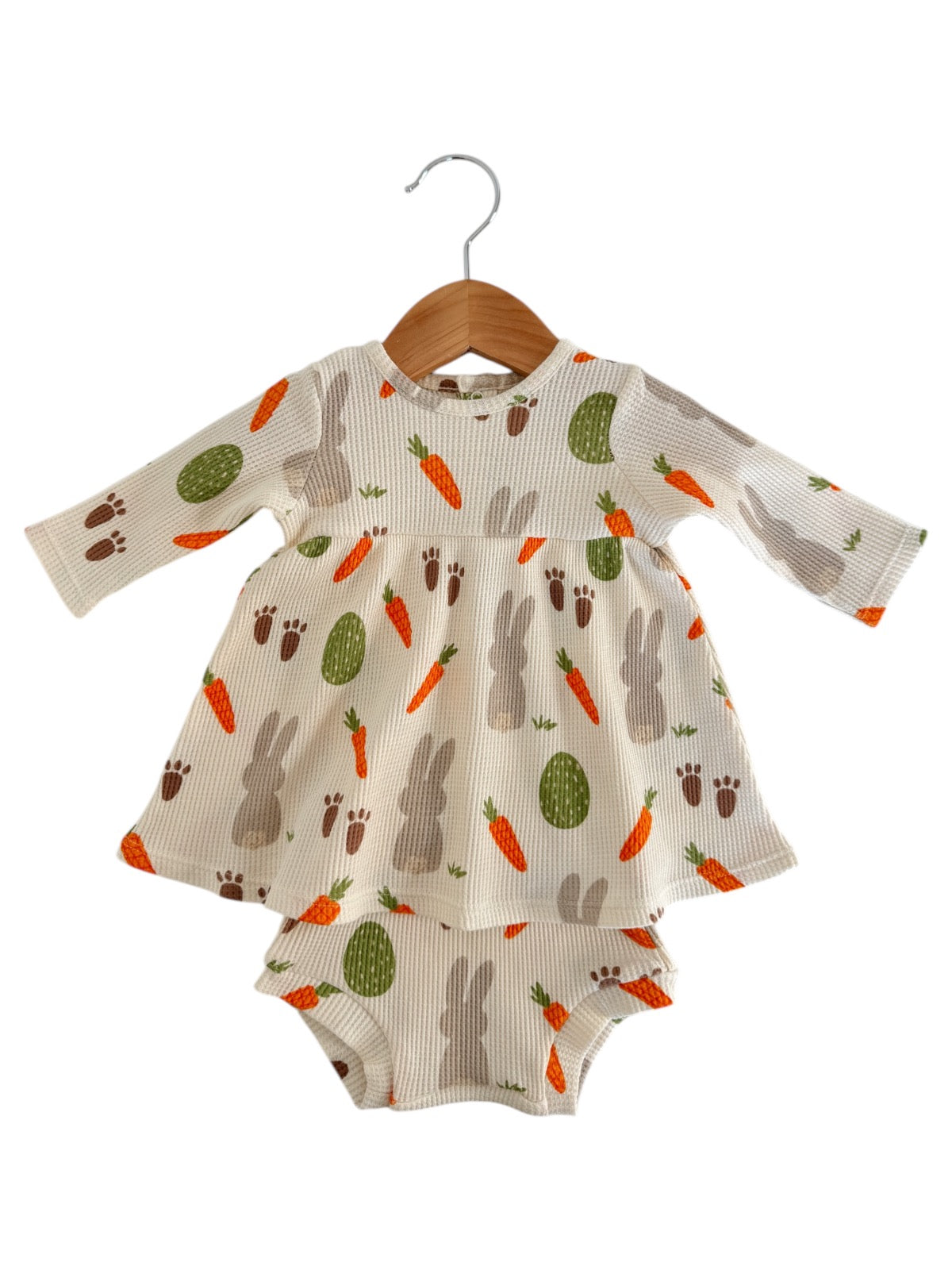 Ribbed baby dress with bunny and carrot patterns, featuring long sleeves and matching bottom, hanging on a wooden hanger.